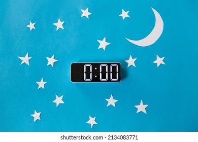 bedtime, sleeping and night time concept - close up of electronic alarm clock showing midnight hour on blue paper background with moon and stars