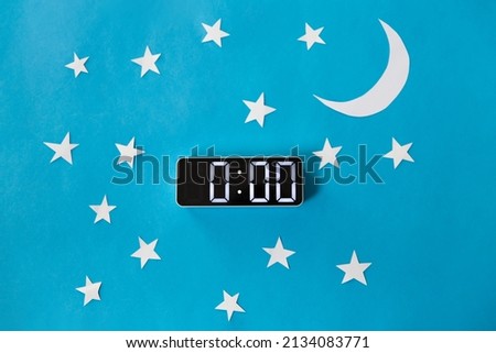 bedtime, sleeping and night time concept - close up of electronic alarm clock showing midnight hour on blue paper background with moon and stars