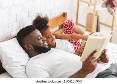 Bedtime Story. Caring African Dad Reading Book To His Daughter At Bedroom, Free Space