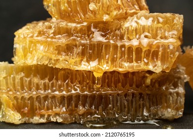 Bee Honeycomb Wax With Honey On Black Background. Honey Dripping From Honey Comb Close Up.