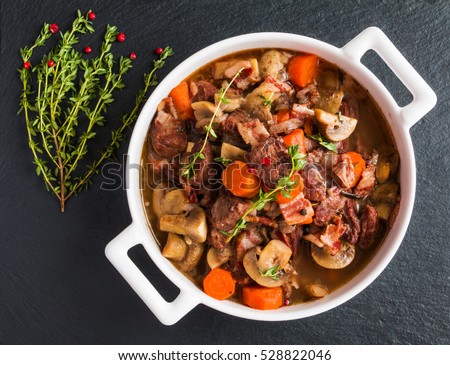 Beef Bourguignon in a casserole on black stone. Stewed with bacon, garlic, carrots, onions, mushrooms,  red wine, fresh thyme and spices. Top view
