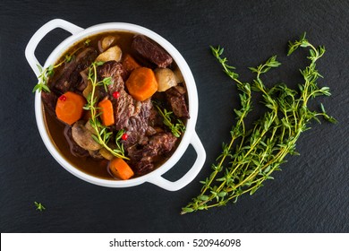 Beef Bourguignon in a white soup bowl on black stone background, top view. Stew with carrots, onions, mushrooms, bacon, garlic and bouquet garni. The dish is served with fresh thyme. - Powered by Shutterstock