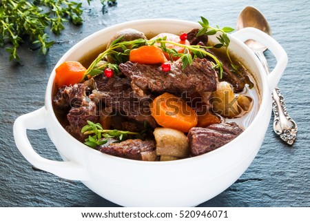 Beef Bourguignon in a white soup bowl on black stone background. Stew with carrots, onions, mushrooms, bacon, garlic and bouquet garni. The dish is served with fresh thyme.