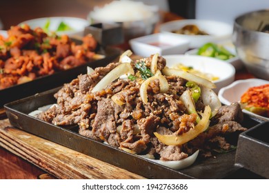 Beef bulgogi close up Korean BBQ dinner on a wooden table with other foods blurred in the background.