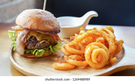 Beef Burger With America Cheese And Bacons On Top Served With Curly Fries On Wooden Board