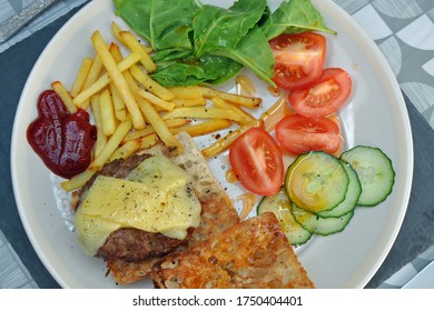 Beef Burger And Chips On A Plate Including A Bread Bun, Melted Cheddar Cheese, Spinach Leaves, Tomatoe Cucumber And Ketchup. Authentic Home Prepared Meal, Lunch Or Dinner. Top Down View