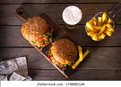 Beef Burger In Classic American Style With Hot Grilled Patty, Melted Cheese On Top, Tomato, Onion, Sauce And Fried Chips Served With Glass Of Beer. View From Above, Top View