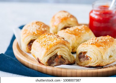 Beef and caramelised onion sausage rolls on a wooden plate with vegemite sauce