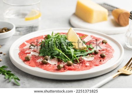 Beef carpaccio with capers, arugula and parmesan on a white plate, selective focus