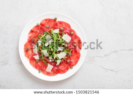 Beef Carpaccio cold appetizer with parmesan, capers and arugula on white plate.Top view.