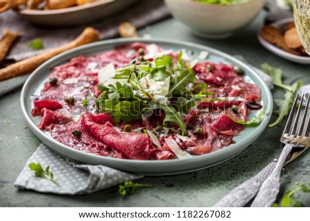 Beef carpaccio on black plate with mustard and parmesan