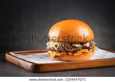 Beef cheese burger on wooden plate with grey background.