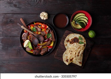 Beef fajita with bell peppers. Tortillas, avocado, sauce served with grilled beef and vegetables on skillet. Tex-mex cuisine