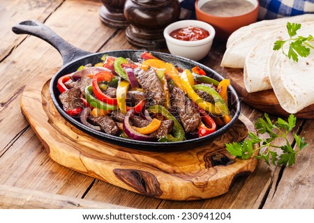 Beef Fajitas with colorful bell peppers in pan and tortilla bread and sauces