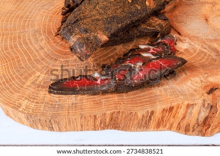 Beef jerky slices are placed on wooden board to larger piece of whole cured beef