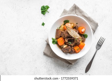 Beef meat stewed with potatoes, carrots and spices on white background, top view. Homemade winter comfort food - slow cooked meat stew in bowl.