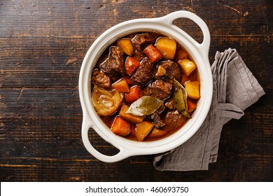 Beef meat stewed with potatoes, carrots and spices in ceramic pot on wooden background - Shutterstock ID 460693750
