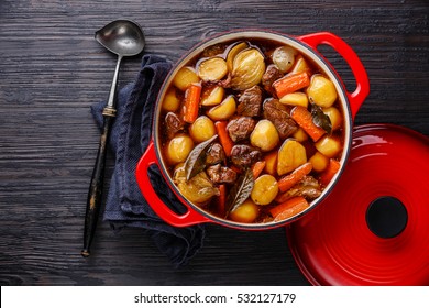 Beef meat stewed with potatoes, carrots and spices in cast iron pot on burned black wooden background