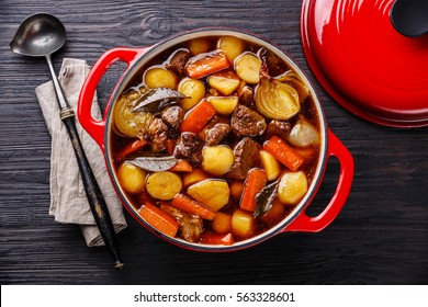 Beef meat stewed with potatoes, carrots and spices in cast iron pot on burned black wooden background