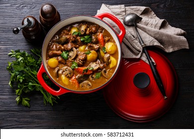 Beef meat stewed with potatoes, carrots and spices in cast iron pan on burned black wooden background