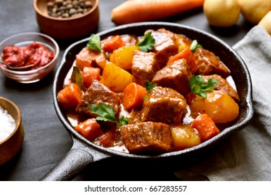 Beef meat stewed with potatoes and carrots in cast iron pan, close up view.