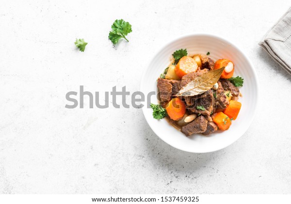 Beef meat stewed with potatoes, carrots and\
spices on white background, top view, copy space. Homemade winter\
comfort food - slow cooked meat\
stew.