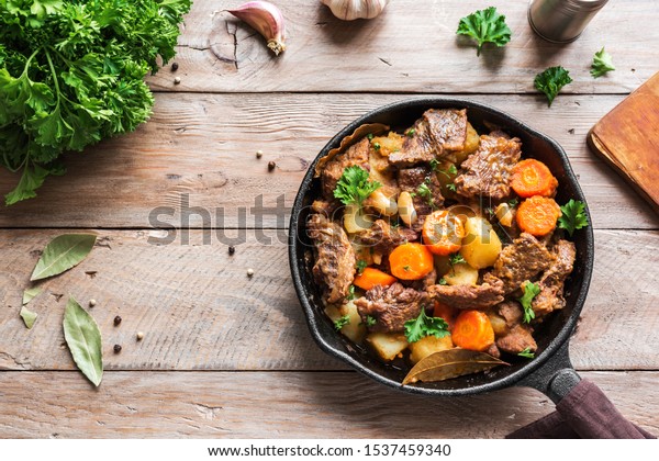 Beef meat stewed with potatoes, carrots and\
spices on wooden background, top view, copy space. Homemade winter\
comfort food - slow cooked meat\
stew.
