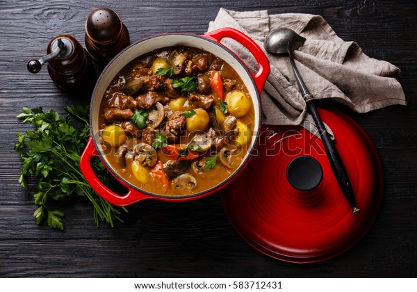 Beef meat stewed with\
potatoes, carrots and spices in cast iron pan on burned black\
wooden background