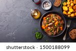 Beef meat and vegetables stew in black bowl with roasted baby potatoes. Dark background. Copy space. Top view.