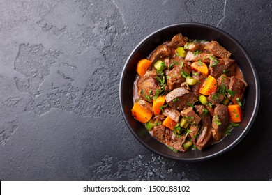 Beef meat and vegetables stew in black bowl. Dark background. Copy space. Top view.