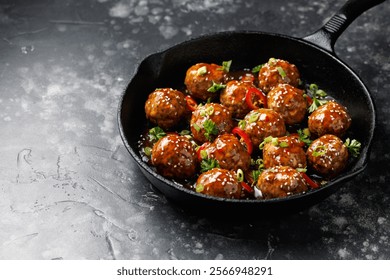 Beef meatballs in teriyaki sauce with sesame seeds, chili and herbs in a cast iron pan.