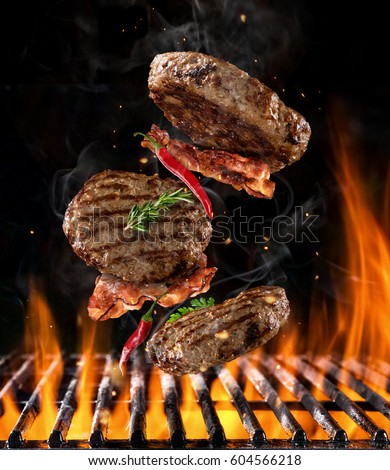 Beef milled meat on hamburger with chilli peppers and bacon, flying above grill with flames on black background