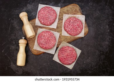 Beef Pork Burgers And Spice Mill On Wooden Board, Top View. Raw Ground Beef Meat Steak Burger Cutlets On Black Table Background, Overhead View. Homemade Uncooked Beef Burgers For Barbecue Grilling.