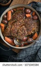 Beef Pot Roast With Red Potatoes And Carrots In Dutch Oven With Vintage Ladle On Rustic Cutting Board.