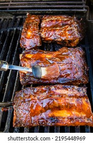Beef Ribs Being Basted With Bbq Sauce On A Grill With A Basting Brush 