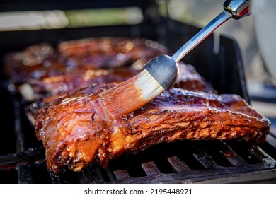 Beef ribs being basted with bbq sauce on a grill with a basting brush  - Shutterstock ID 2195448971