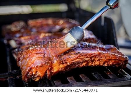 Beef ribs being basted with bbq sauce on a grill with a basting brush 