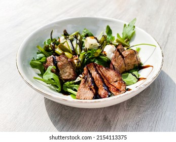 Beef roasted meat with balsamic vinegar, green beans, and arugula on a white plate. Plate. Beef. Cooked. Steak. Grilled. Delicious. Dish. Roast. Lunch. Roasted. Salad. Gourmet. Organic