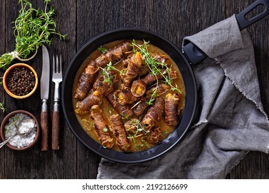 Beef Rouladen Filled With Mustard, Pickles, Carrot And Onions In Beef Gravy In Pan On Dark Wooden Table With Thyme And Cutlery, Horizontal View From Above, Flat Lay