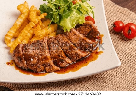 Beef slice meltic saikoro served on a white plate with french fries placed on a wooden table with sauce, burlap, tomatoes, fork and knife as garnish.