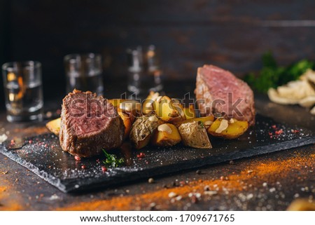 Beef sous vide with baked potato slices served on black stone on craft brown and green background with ingredients among it