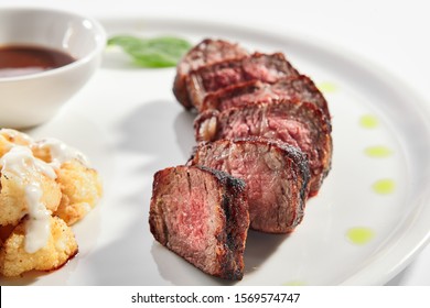 Beef Steak With Cauliflower Dish Top View. Baked Meat Alternative Cuts With Peppercorn Sauce. Roasted Pork Piece Isolated On White Background. Gourmet Meal Garnished With Herbs On Plate Composition