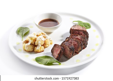Beef Steak With Cauliflower Dish Top View. Baked Meat Alternative Cuts With Peppercorn Sauce. Roasted Pork Piece Isolated On White Background. Gourmet Meal Garnished With Herbs On Plate Composition