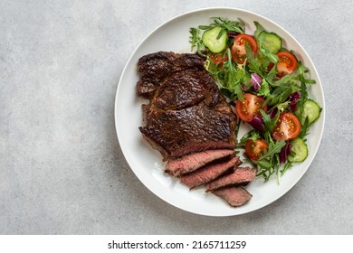 beef steak with fresh vegetable salad on white plate, top view, copy space