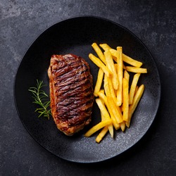 Beef Steak Medium Rare With French Fries On A Black Plate. Grey Background. Close Up. Top View.