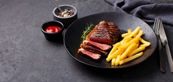Beef Steak Medium Rare With French Fries On A Black Plate. Grey Background. Close Up. Copy Space.