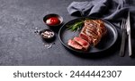 Beef Steak medium rare on a black plate. Grey background. Close up. Copy space.