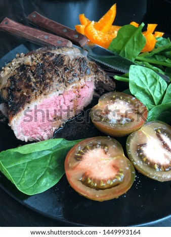 Beef steak medium rare with spinach, tomatoes and sweet yellow pepper on the black plate.