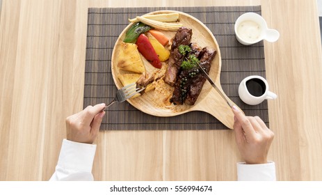 Beef Steak on wooden plate with woman hands.