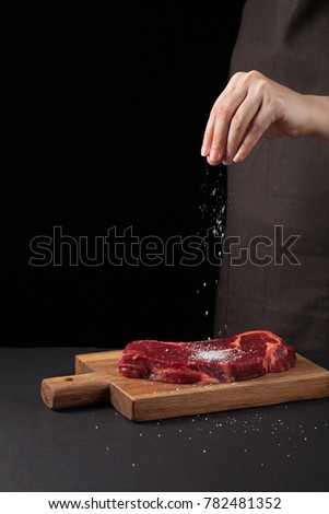 Beef steak and salt by chef on the background with free space for text design or logotype menu restaurant. Vertical photo. Food background. Black text area. Copy space.